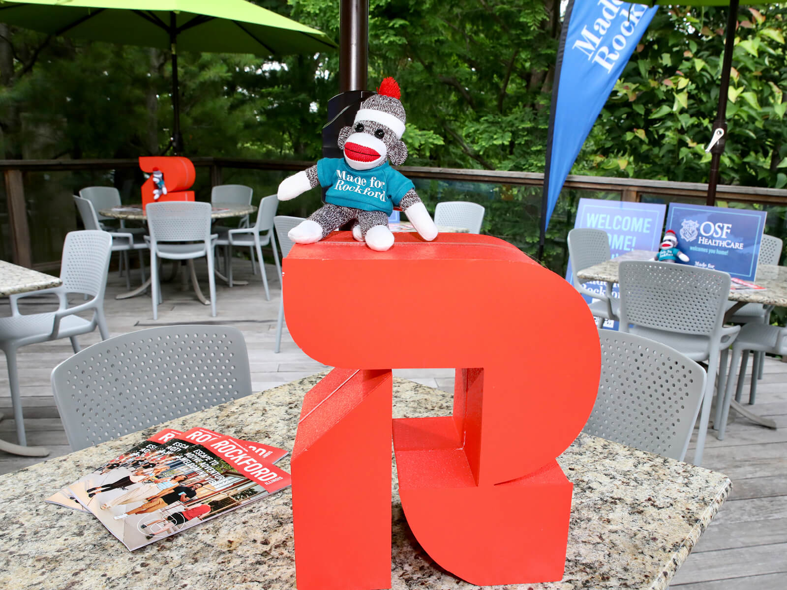 A sock monkey wearing a Made for Rockford shirt sitting on the GoRockford logo