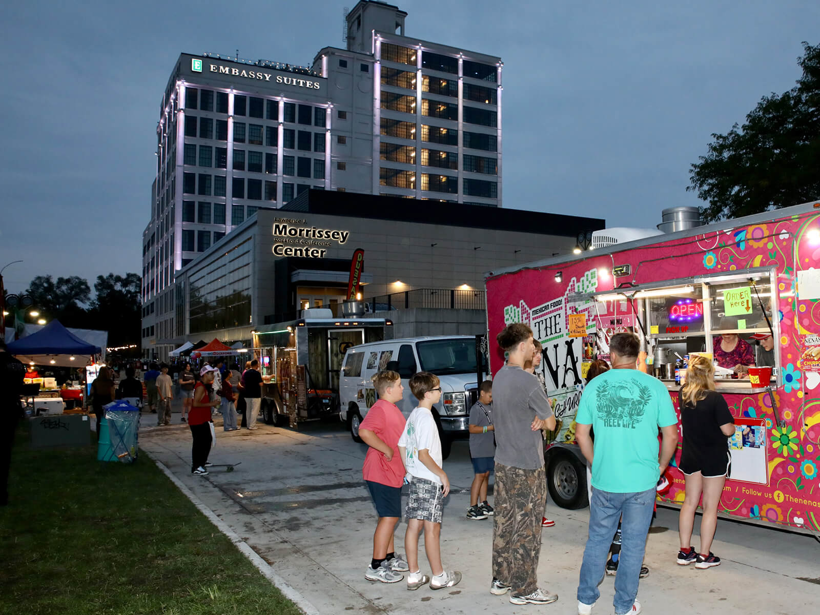 Evening food truck outside the Embassy Suites and Morrissey Conference Center, with families, colorful vendors, and lively crowds.