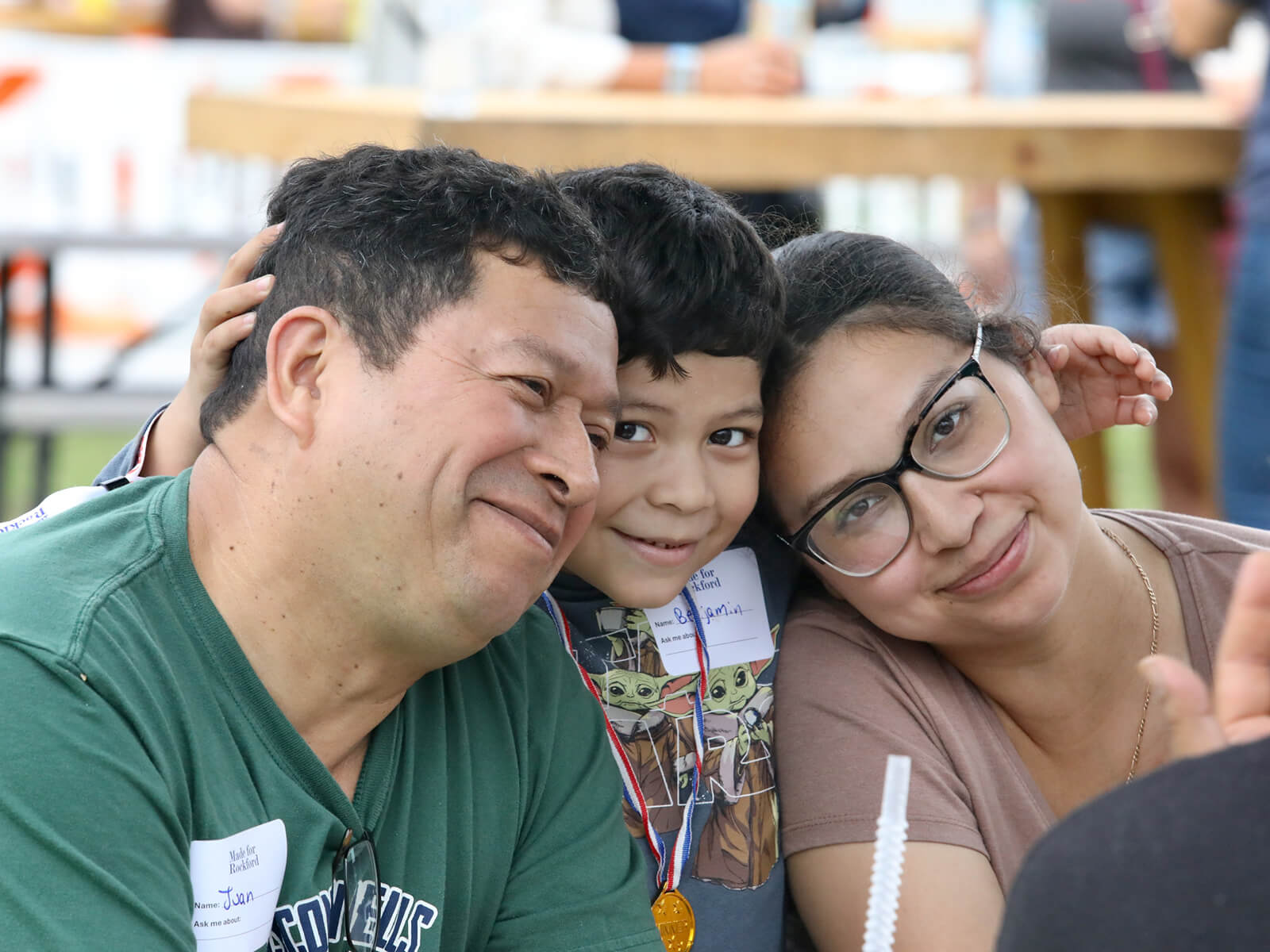 Smiling family poses closely for a selfie at RockYard Music Fest; a young boy wearing a medal stands between his parents, conveying warmth and joy.