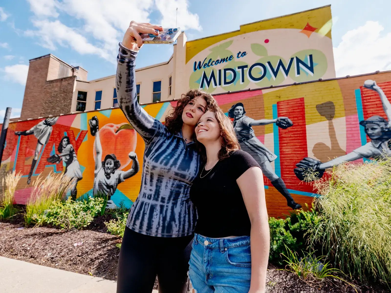 Friends posing for a selfie in front of the Rockford Midtown Peaches mural